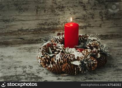 Burning candle in a Christmas wreath with seasonal decorations.