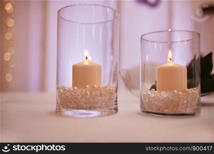 Burning candle in a round glass candlestick with decorative seashells. candles on a glass candlestick. candles on a glass candlestick. Burning candle in a round glass candlestick with decorative seashells