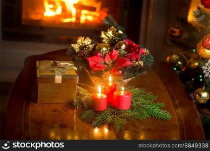 Burning candles by the decorated Christmas tree, giftbox and traditional wreath