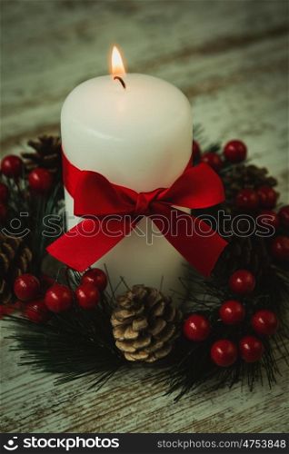 Burning candles in a Christmas wreath with seasonal decorations.