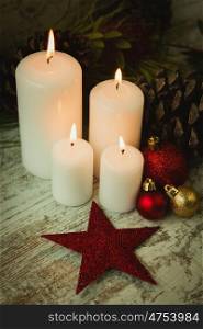 Burning candles in a Christmas wreath with seasonal decorations.