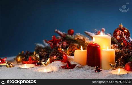 Burning christmas candles with red and golden decorative stars , baubles , pine cones and green branches on snow. Christmas candles with decoration