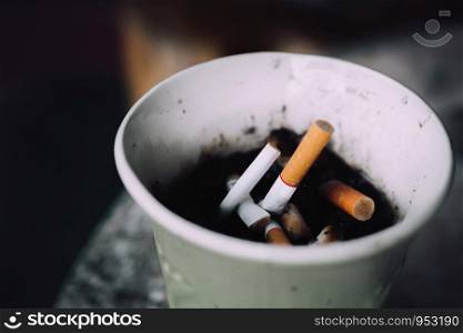 Burning cigarettes in ashtray on background. Area for smoking have cigarette stub on paper cup.