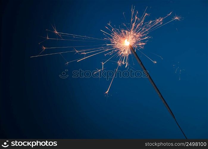 Burning festive Christmas sparkler on blue background with a lot of sparks