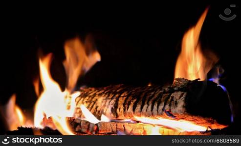 Burning log in fireplace on dark black background closeup.