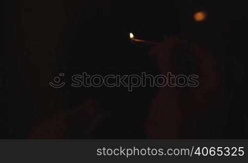 Burning match in man&acute;s hand on black background