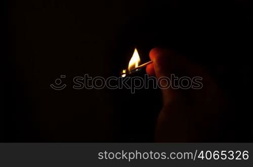 Burning match in man&acute;s hand on black background