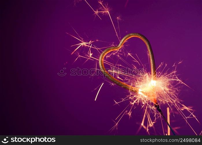 Burning sparkler in love heart shape on a purple background with lots of sparks. Valentine&rsquo;s day celebration.