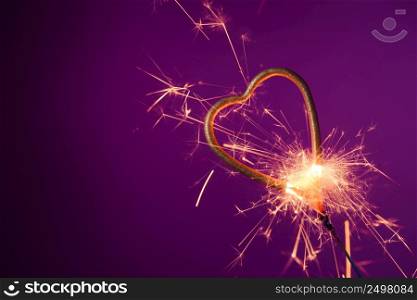 Burning sparkler in love heart shape on a purple background with lots of sparks. Valentine&rsquo;s day celebration.