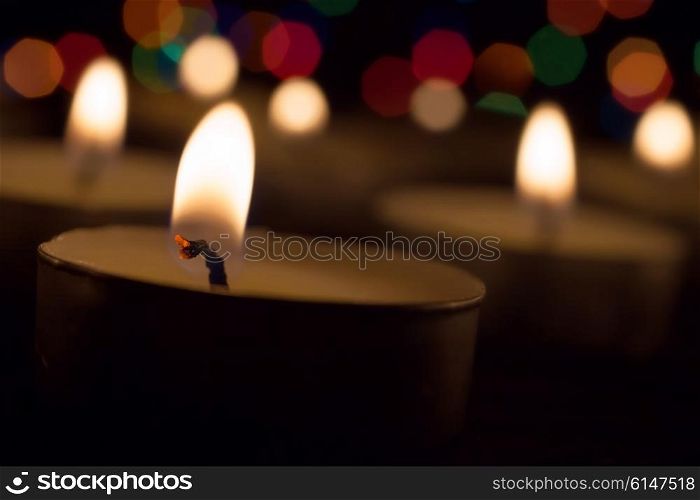 Burning tea candle against the backdrop of colored lights
