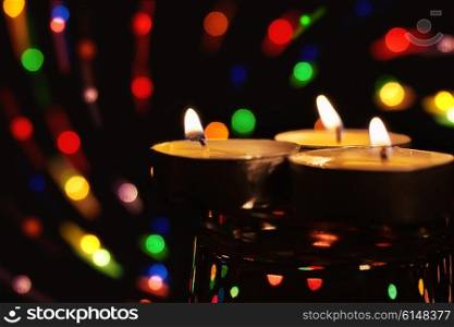 Burning tea candle against the backdrop of colored lights