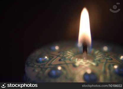 burning white candle with green ornament and pearls on the dark background