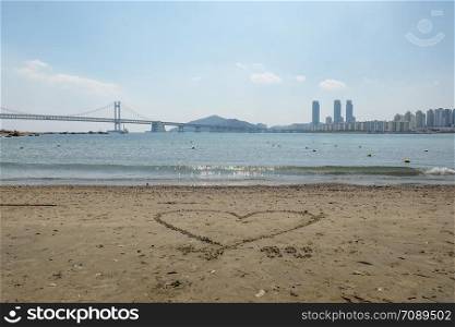 Busan Gwangan bridge taken from Gwangalli beach in brightday with blue sky and heart shape on the beach.
