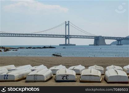 Busan Gwangan bridge taken from Gwangalli beach in brightday with blue sky and many boats on the beach.