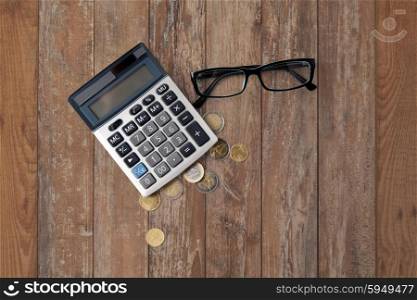 busines, finance, money and bookkeeping concept - calculator, eyeglasses and euro coins on wooden table background