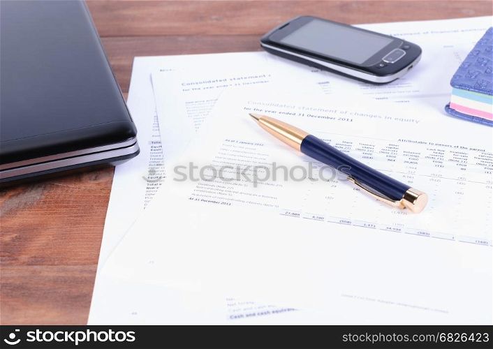 business accessories - a pen, a phone and laptop on Desk with financial documents. Pen, laptop and mobile phone lying on tax and financial documents