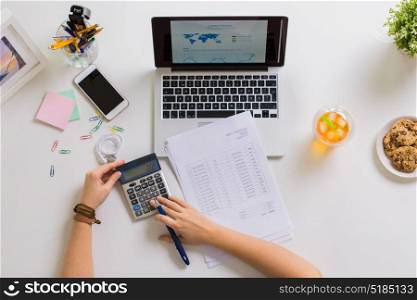 business, accounting and freelance concept - woman hands with calculator, papers and laptop computer working at office. hands with calculator and papers at office table