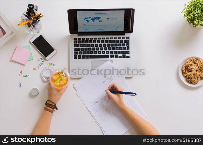 business, accounting and freelance concept - woman hands with papers, cup of drink and laptop computer working at office table. woman hands with papers and cup of drink at office