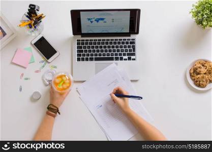 business, accounting and freelance concept - woman hands with papers, cup of drink and laptop computer working at office table. woman hands with papers and cup of drink at office
