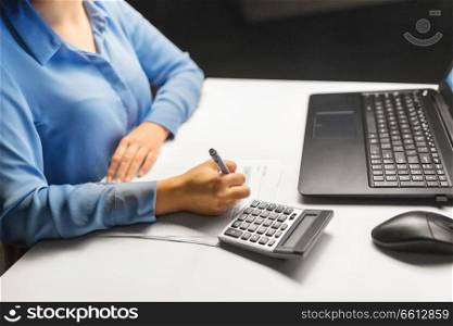 business, accounting, deadline and overwork concept - close up of businesswoman with tax form, laptop computer and calculator working at night office. businesswoman with papers working at night office
