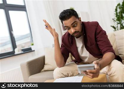 business, accounting, finances and people concept - confused man with papers and calculator at home. confused man with papers and calculator at home