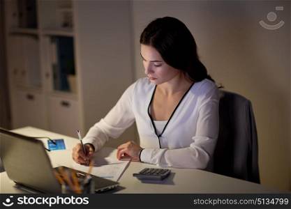 business, accounting, overwork, deadline and people concept - woman with tax form and calculator working at night office. woman with calculator and papers at night office. woman with calculator and papers at night office