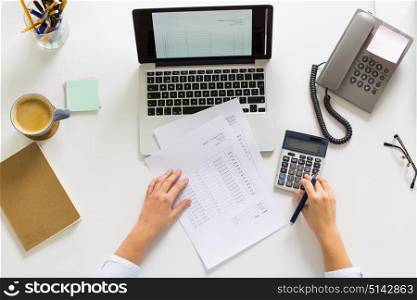business, accounting, people and technology concept - hands of businesswoman with calculator, papers and laptop computer working at office. hands with calculator and papers at office table
