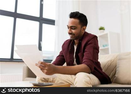 business, accounting, taxes and people concept - man with calculator reading papers at home. man with papers and calculator at home