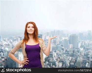 business, advertising and people concept - smiling teenage girl in casual clothes holding something on her palm over city background