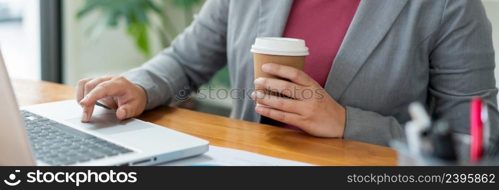 Business analyst concept the female officer holding a cup of coffee typing information on the computer laptop.