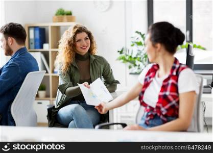 business and creative people concept - female office workers giving each other papers. female office workers giving each other papers. female office workers giving each other papers