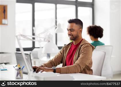 business and creative people concept - happy smiling young indian man with laptop computer working at office. happy indian man with laptop computer at office. happy indian man with laptop computer at office