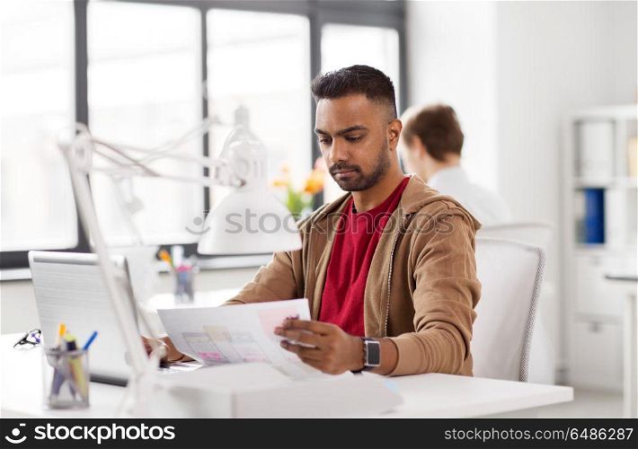 business and creative people concept - young indian man with laptop computer and papers working at office. indian man with laptop computer at office. indian man with laptop computer at office