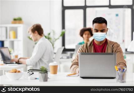 business and creative people concept - young indian man with laptop computer wearing protective medical mask for protection from virus disease working at office. indian man with laptop in medical mask at office