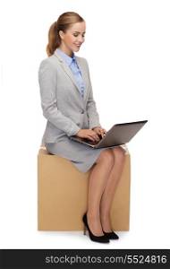 business and delivery service concept - smiling woman sitting on cardboard box with laptop computer