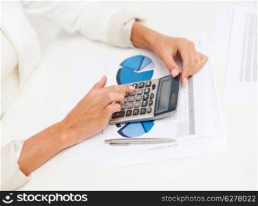business and education concept - businesswoman with calculator, charts and graphs in office