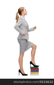 business and education concept - smiling businesswoman stepping on pile of books