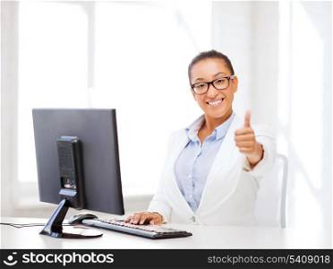 business and internet concept - smiling african businesswoman with computer in office showing thumbs up