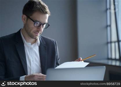 Business and job concept. Serious male professional analyzing documents at workplace, working on laptop computer in office, focused german businessman wearing glasses and black suit. Serious male professional analyzing documents at workplace. Business and job concept