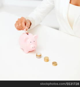 business and money saving concept - close up of female hand putting euro coins into piggy bank in office