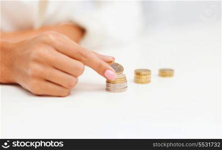 business and money saving concept - close up of female hand putting euro coins into columns in office