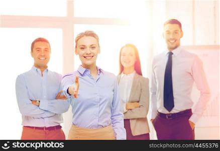 business and office concept - smiling beautiful businesswoman ready for handshake with team in office. smiling businesswoman in office with team on back