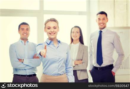 business and office concept - smiling beautiful businesswoman ready for handshake with team in office. smiling businesswoman in office with team on back