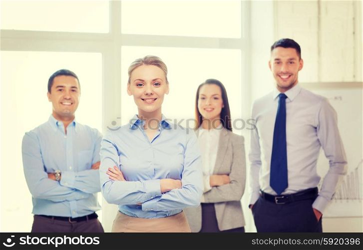 business and office concept - smiling beautiful businesswoman with crossed hands and team in office. smiling businesswoman in office with team on back