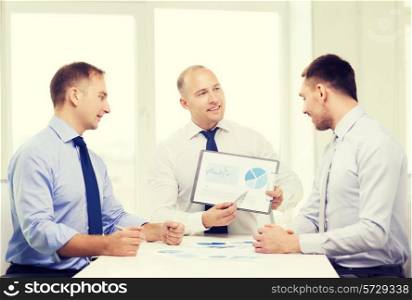 business and office concept - smiling businessman showing others charts in office