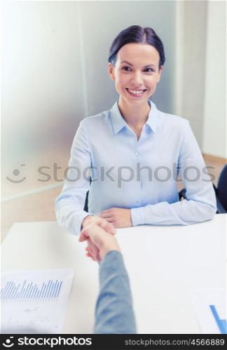 business and office concept - smiling businesswoman shaking hand in office. smiling businesswoman shaking hand in office