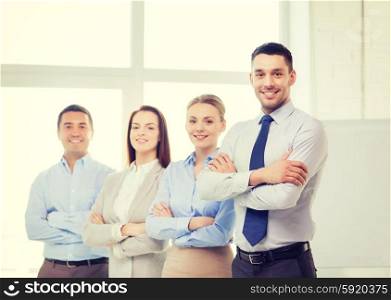 business and office concept - smiling handsome businessman with crossed hands and team in office. smiling businessman in office with team on back