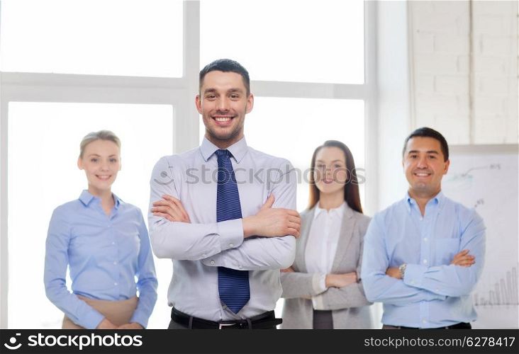business and office concept - smiling handsome businessman with crossed hands and team in office