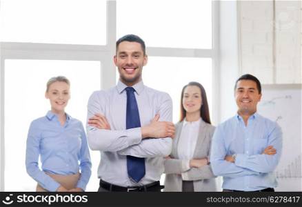 business and office concept - smiling handsome businessman with crossed hands and team in office