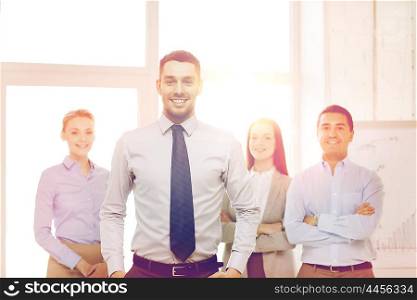 business and office concept - smiling handsome businessman with team in office. smiling businessman in office with team on back